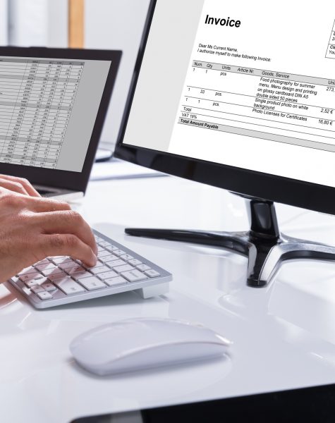 Close-up Of A Businessperson's Hand Checking Invoice On Computer At Workplace