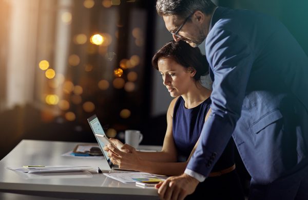 Shot of a coworkers using a smartphone while woking late in the office